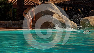 Boy and girl in swimming suits are jumping into the pool outdoors