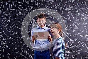 Boy and girl with tablet against big blackboard, school