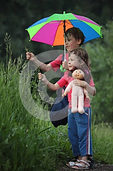 Boy and girl under umbrella in park tear grass