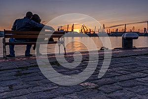 Boy and girl watches the sunset at the sea station with ships.