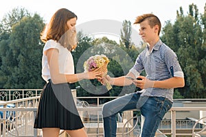 Boy gives girl bouquet of flowers. Outdoor portrait of couple teenagers, sunny summer day