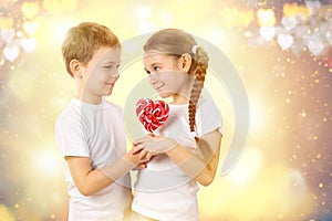 Boy gives a little girl candy red lollipop in heart shape. Valentine`s day