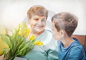 Boy giving a bunch of yellow flowers tulipan to grandmother. Grandson and grandma spending  time together.  Kindness to senior. photo