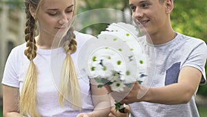 Boy giving flowers to pretty girl, pleasant surprise, first love in adolescence