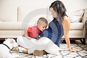 Boy Giving A Kiss On Pregnant Mother`s Abdomen At Home