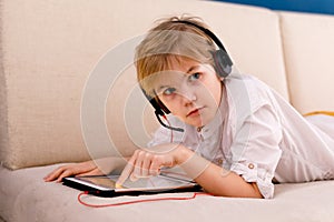 A boy with glasses and headphones is learning lessons with a tablet and books. Home distance learning online