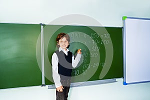 Boy with glasses holds chalk near blackboard