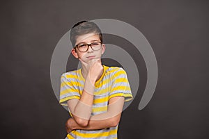 a boy with glasses looks thoughtfully into the distance on a dark gray background.