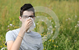 Boy with glasses sneezing on a white handkerchief outdoors becau photo