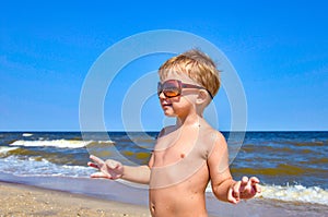 A boy in glasses stands on the beach by the sea