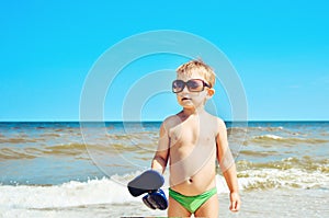 A boy in glasses stands on the beach by the sea