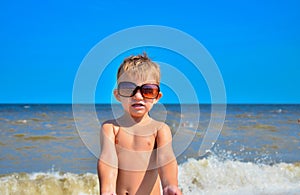 A boy in glasses stands on the beach by the sea