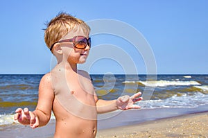 A boy in glasses stands on the beach by the sea