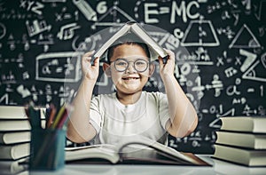 A boy with glasses studied and put a book on his head in the classroom