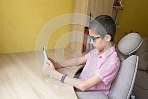 Boy in glasses studying homework with electronic book during his online lesson. Quarantine. Distance learning. Remote education.