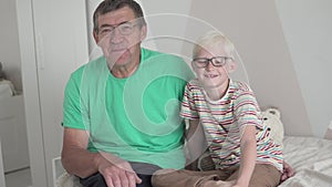 A boy with glasses talks to his grandfather at home on the couch