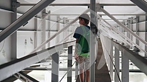 The boy goes along a long metal corridor under the bridge.