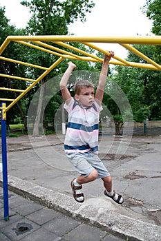 Boy goes in for sports in the summer outside on the playground, walking on the horizontal bars