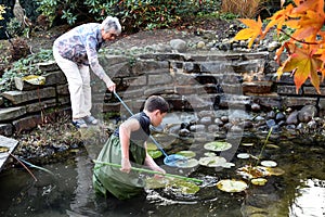 Boy and grandmother cleaning garden pond