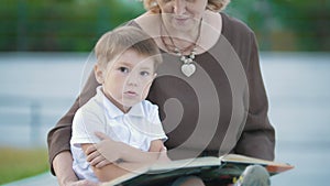 Boy and grandmother read book in the park on the bench