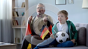 Boy and grandpa holding German flags, watching football, worrying about game