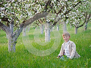 Boy on the grass near blooming apple trees in the garden