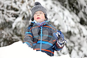 Boy with gray stocking cap and color striped jacket playin on the snow pile