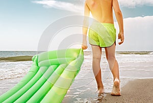 Boy with green swimming mattress stands on seasurf line