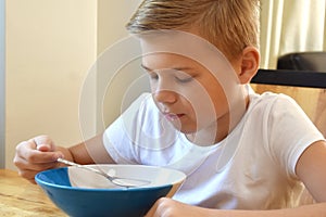 Boy doesn`t want to eat. Unhappy child at the kitchen table. Tasteless food.