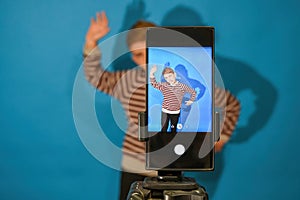 The boy grimaces and poses on a mobile camera in the studio to download and watch funny videos