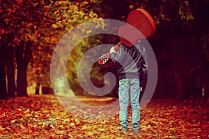 Boy with guitar walking on the autumn road. Back view.