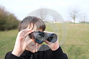 Boy, guy 8-10 years old stalker looks through black binoculars in the park, spies, hunts down secrets, the concept of surveillance