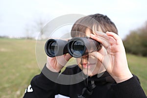 Boy, guy 8-10 years old stalker looks through black binoculars in the park, spies, hunts down secrets, the concept of surveillance