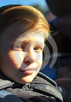 A boy with half-lighted face looking to the camera. Boy`s face in the sunset light.