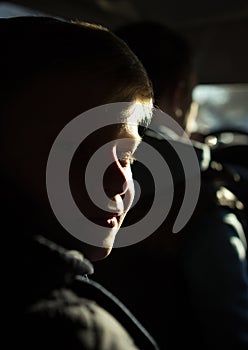 A boy with half-lighted face looking to the camera. Boy`s face in the sunset light.