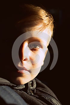 A boy with half-lighted face looking to the camera. Boy`s face in the sunset light.