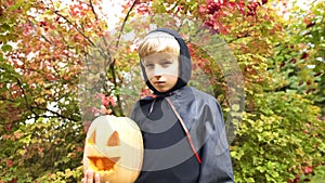 Boy in Halloween costume holding pumpkin jack-o-lantern, alone in forest, spooky