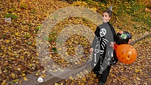 A boy in a Halloween costume walks along a path covered with yellow leaves