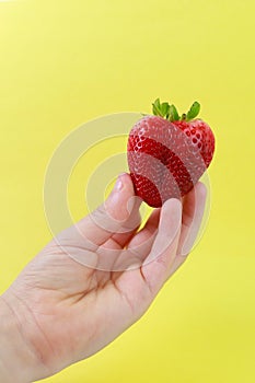 A boy hand holding a heart shapes strawberry on yellow background