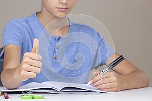 Boy hand holding pen in left hand and writing in a notebook, doing homework. Thumb up hand gesture. Left Handers Day