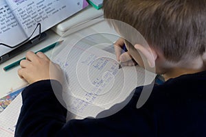 Boy with pencil writing english words by hand on traditional white notepad paper.