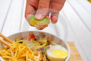 Boy hand squeezing lime on Malay Mee Rebus in the bowl with chopsticks on white table This dish is made of noodles ,vegetable,egg