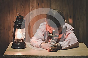 Boy hands holding a holy cross praying to God In the dark and with the lamp beside, Child Praying for God Religion