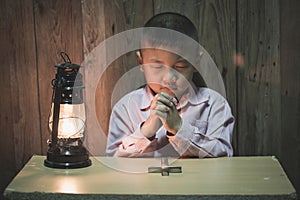 Boy hands praying with a holy cross In the dark and with the lamp beside, Child Praying for God Religion