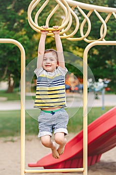 Boy hanging on monkey bars in park on playground.