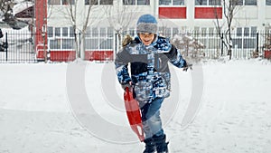 Boy happily running with plastic sleds in the snow, enjoying the fresh air and winter scenery