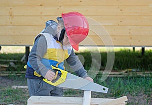Boy in hard hat with a handsaw sawing a wooden Board