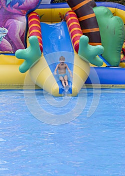 Boy has into pool after going down water slide during summer. little boy sliding down water slide and having