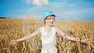 Boy in a hat walks on a golden wheat field on a sunny day