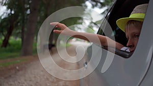 boy in hat waves from traveling car outside city. Traveling by car. Freedom, vacation. pleasure of relaxation. long trip